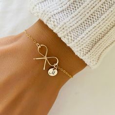 a woman's arm with a gold bracelet and initial charm