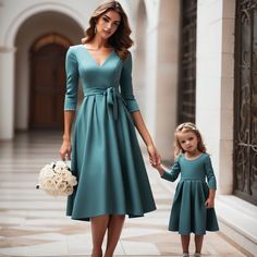 a mother and daughter dressed in teal dresses holding hands while walking down the hall