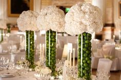 white flowers and greenery are arranged in tall vases on the dining room table