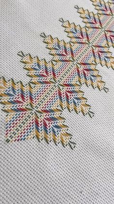 a cross stitch pattern on the back of a white tablecloth with red, yellow and blue designs