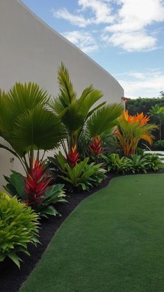 an outdoor area with green grass, plants and flowers on the side of a building