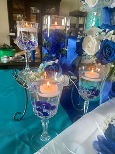 three candles are lit in glass vases on a table with blue and white flowers