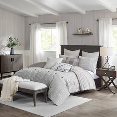 a large bed sitting in a bedroom on top of a hard wood floor next to two windows