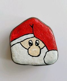 a painted rock with a santa claus face on it's side, sitting on a white surface