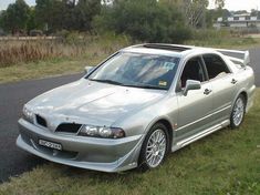 the silver car is parked on the side of the road in front of some grass