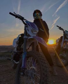 a person sitting on a dirt bike with the sun setting in the distance behind them