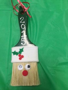 a small brush with a face on it and holly decorations hanging from the top, against a green background