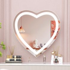 a white heart shaped mirror sitting on top of a table next to a vase and lamp