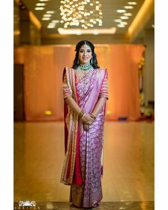 a woman in a pink and gold sari posing for the camera with her hands on her hips