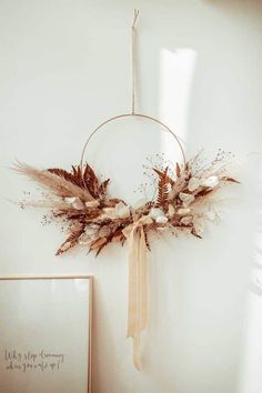 a wreath hanging on the wall with dried flowers and leaves in it next to a framed photograph