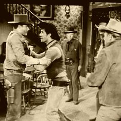 an old black and white photo of men in western wear talking to each other on the set of a television show