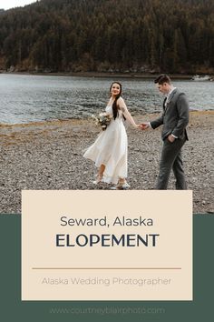 a bride and groom holding hands on the shore of a lake with mountains in the background