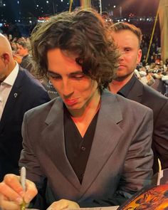 a man in a suit writing on a piece of paper at a table with other people