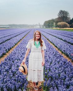 a woman in a white dress and hat standing in a field full of purple flowers