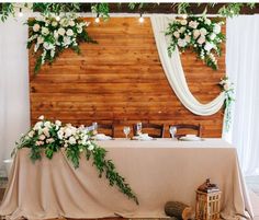 the table is set up with flowers and greenery for an elegant wedding reception in front of a wood paneled wall