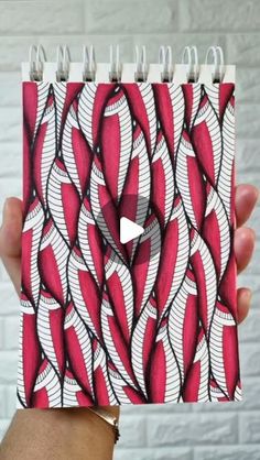 a hand holding up a spiral notebook with red and white designs