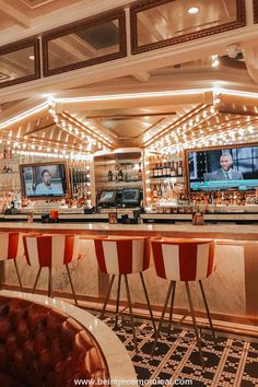 a bar with red and white striped chairs in front of the televisions on the wall