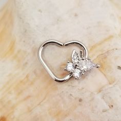 a heart shaped diamond ring on top of a marble slab with a butterfly in the middle