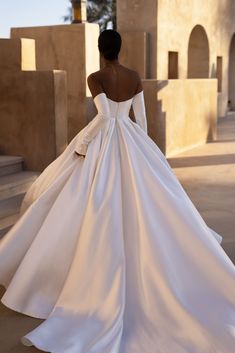 a woman in a white wedding dress is walking down the street with her back to the camera