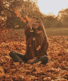 a woman is sitting in the leaves with her hands up to her face and eyes closed