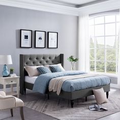 a bed room with a neatly made bed next to a chair and two tables in front of a large window