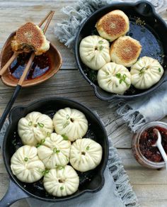 two pans filled with dumplings on top of a wooden table next to sauce