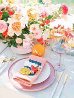 the table is set with pink and orange plates, silverware, and napkins