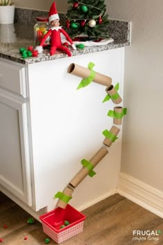 an elf is sitting on the counter next to a roll of toilet paper and a christmas tree