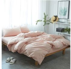 an unmade bed with pink sheets and pillows in a white room next to a window