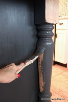 a woman's hand holding a paint brush near a black cabinet