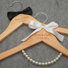 two personalized wooden hangers with white pearls and black bows are on the floor