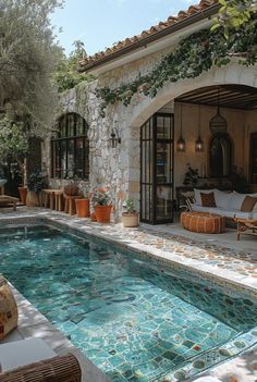 an outdoor swimming pool with patio furniture and plants on the wall, surrounded by greenery