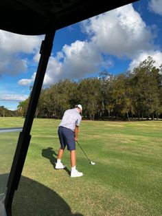 a man is playing golf on the green with trees in the background and clouds in the sky