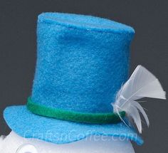 a blue top hat with white feathers and a green ribbon on the side, sitting on a doll's head