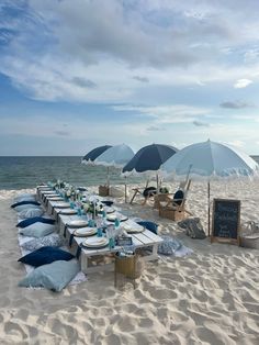 an empty table set up on the beach with blue and white umbrellas in the background