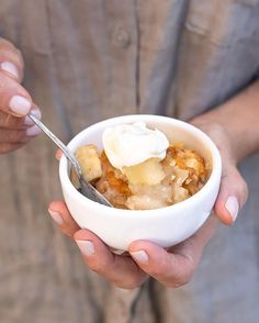 a person is holding a bowl of food with a spoon in it and some whipped cream on top