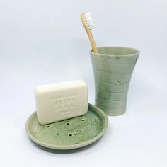 a toothbrush in a cup next to a soap bar on a saucer and plate