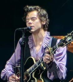 a young man with curly hair playing an acoustic guitar on stage at a music festival