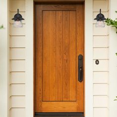 a wooden door on the side of a white house with two black lights above it