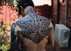 a man with a black and white tattoo on his back is standing in front of a building