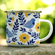 a blue and yellow bird painted on a white coffee mug sitting on a wooden table