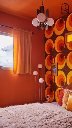 a bedroom decorated in orange and yellow with circles painted on the wall behind the bed