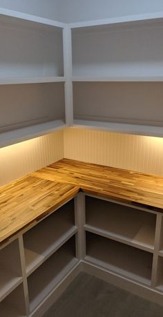 an empty room with white shelves and wood counter tops in the corner between two walls