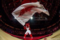 a man in red and white uniform holding a flag on top of a basketball court