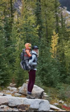 a man and woman hiking in the mountains with backpacks on their back, one carrying a child