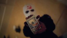 a person holding up a dollar bill in front of a white mask on the wall