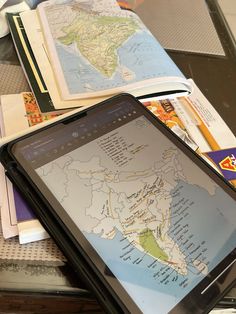 a tablet computer sitting on top of a table covered in books and papers next to a map