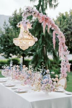 a long table with pink flowers and chandelier hanging from it's ceiling