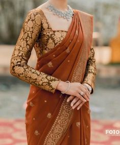 a woman wearing an orange sari with gold and silver jewelry on her neck, standing in