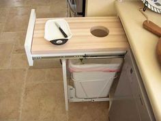 a kitchen counter with a cutting board on it and a trash can under the sink